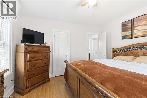 Hardwood flooring extends throughout this interior space, featuring a ceiling fan, white paneled doors, and a window with white blinds - 134 Queensway Drive, Brantford, ON 