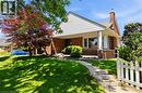 Brick and siding exterior featuring a covered front porch with white pillars, a paved walkway, a picket fence, and mature landscaping - 134 Queensway Drive, Brantford, ON 