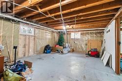 Unfinished basement space featuring exposed wood joists, concrete flooring, two windows, and an insulated wall with vapor barrier - 