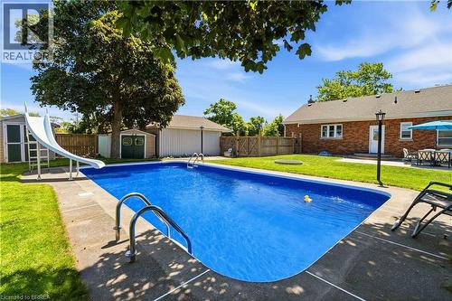 Expansive backyard featuring a rectangular in-ground swimming pool with concrete surround, a white pool slide, and two storage sheds - 134 Queensway Drive, Brantford, ON 