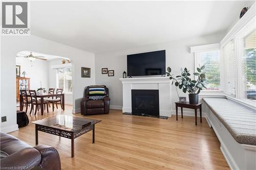 Bright living area featuring wood-finish flooring, a white mantel fireplace, multiple windows with blinds, and an integrated window seat - 134 Queensway Drive, Brantford, ON 