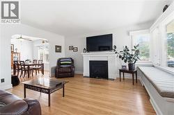 Bright living area featuring wood-finish flooring, a white mantel fireplace, multiple windows with blinds, and an integrated window seat - 