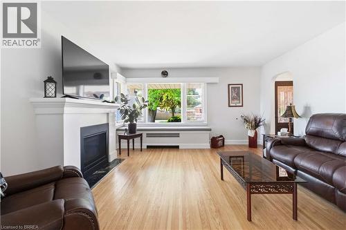 Bright living room featuring wood-finish flooring, a white mantel fireplace with a black surround, and a large multi-pane window with blinds - 134 Queensway Drive, Brantford, ON 