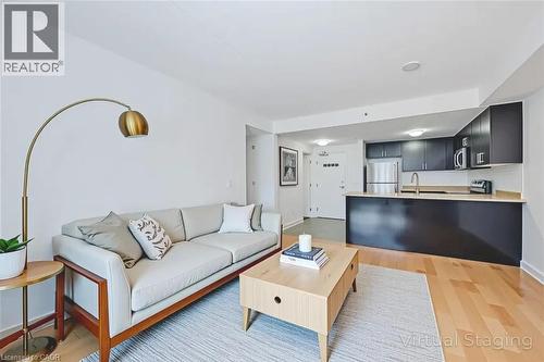 Open-concept living space featuring wood-finish flooring, recessed lighting, and a kitchen with dark cabinetry and stainless steel appliances - 41 Goodwin Drive Unit# 202, Guelph, ON 