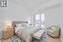 Bright bedroom featuring a large window, light-toned wood-finish flooring, and white walls - 