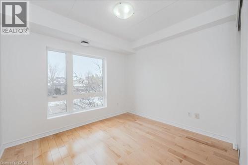 Bright room featuring wood-finish flooring, white baseboards, and a large multi-pane window - 41 Goodwin Drive Unit# 202, Guelph, ON 