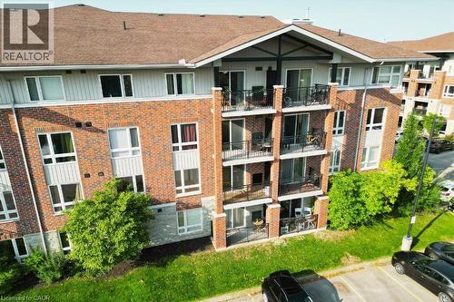 Multi-story residential building featuring a brick exterior with white siding accents and a brown shingle roof - 41 Goodwin Drive Unit# 202, Guelph, ON 
