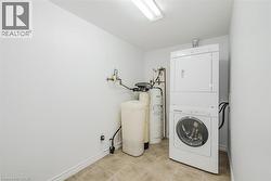 Dedicated utility area featuring a stacked washer and dryer unit, water softener system, and tiled flooring - 