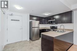 Modern kitchen featuring stainless steel appliances, dark wood-finish cabinetry, a light-toned countertop, and a white tile backsplash - 