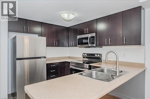 Kitchen featuring stainless steel appliances, dark wood-finish cabinetry, light-toned countertops, a dual-basin sink with a gooseneck faucet, and a white subway tile backsplash - 41 Goodwin Drive Unit# 202, Guelph, ON 