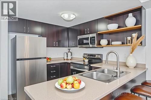 Modern kitchen featuring stainless steel appliances, dark wood cabinetry, light-toned countertops, a dual basin sink with a pull-down faucet, and integrated open shelving - 41 Goodwin Drive Unit# 202, Guelph, ON 
