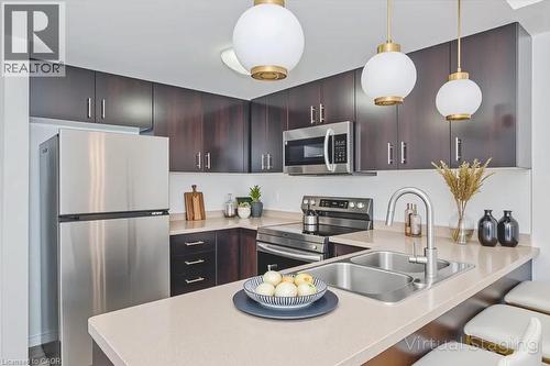 Contemporary kitchen featuring dark wood-finish cabinetry, stainless steel appliances, light-toned countertops, and a dual basin sink - 41 Goodwin Drive Unit# 202, Guelph, ON 