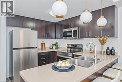 Contemporary kitchen featuring dark wood-finish cabinetry, stainless steel appliances, light-toned countertops, and a dual basin sink - 