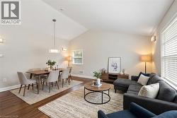 *VIRTUALLY STAGED* Spacious living area featuring vaulted ceilings, wood-finish flooring, recessed lighting, and ample natural light from multiple windows - 