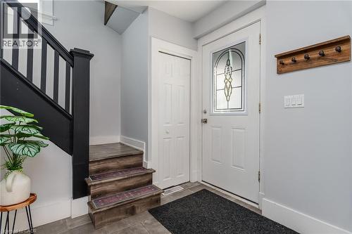 Entry foyer featuring a white paneled door with decorative glass insert, dark wood-finish stairs with black banister, light gray wall paint, and gray square floor tiles - 40 Woodland Avenue, Kitchener, ON 