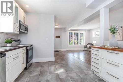 Contemporary kitchen featuring white cabinetry, stainless steel appliances, dark countertops, and a white subway tile backsplash - 40 Woodland Avenue, Kitchener, ON 