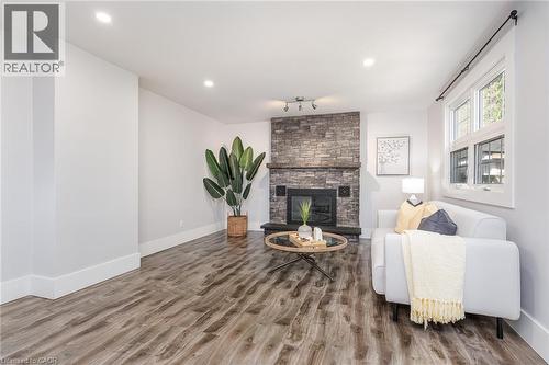 Living area featuring a stone-clad fireplace with a wood mantel, wood-finish flooring, recessed lighting, and a double-pane window - 40 Woodland Avenue, Kitchener, ON 