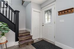 Entry foyer featuring a white paneled door with decorative glass insert, dark wood-finish stairs with black banister, light gray wall paint, and gray square floor tiles - 