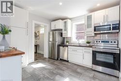Kitchen featuring wood-finish flooring, white cabinetry, stainless steel appliances, a built-in microwave, and a window above the sink - 