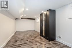 Spacious room featuring wood-finish flooring, recessed lighting, and a dark-toned built-in wardrobe with mirrored panels - 