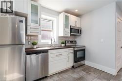 Compact kitchen featuring white cabinetry, stainless steel appliances, a tile backsplash, dark countertops, and gray tile flooring - 