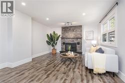 Living area featuring a stone-clad fireplace with a wood mantel, wood-finish flooring, recessed lighting, and a double-pane window - 