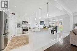 Bright kitchen featuring white cabinetry, stainless steel appliances, a white island with a stone countertop, and pendant lighting - 