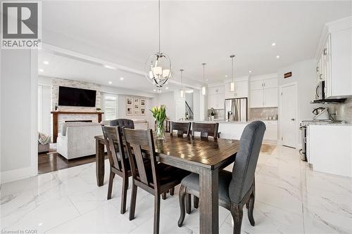Dining area featuring a dark wood-finish table, a contemporary chandelier, and white marble-look tile flooring - 72 Elmbank Trail, Kitchener, ON 