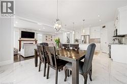 Dining area featuring a dark wood-finish table, a contemporary chandelier, and white marble-look tile flooring - 