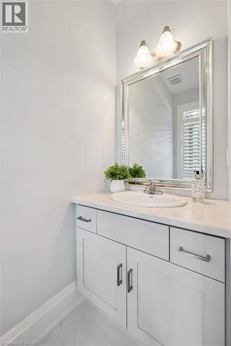 Vanity featuring a white countertop with an undermount sink, white cabinetry with dark hardware, a large framed mirror, and a two-bulb wall sconce - 72 Elmbank Trail, Kitchener, ON 