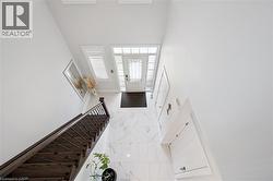 Two-story foyer featuring wood-finish staircase with wrought iron balusters, white marble-look flooring, and a glass-paneled entry door with sidelights - 