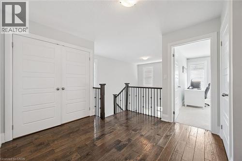 Upper landing featuring wood-finish flooring, white paneled doors, and a staircase with dark wood handrail and black metal balusters - 72 Elmbank Trail, Kitchener, ON 
