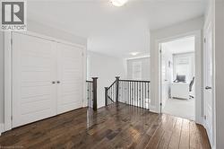 Upper landing featuring wood-finish flooring, white paneled doors, and a staircase with dark wood handrail and black metal balusters - 