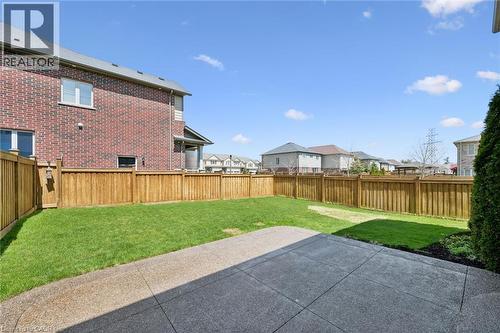 Expansive fenced backyard featuring a concrete patio, manicured lawn, and brick exterior - 72 Elmbank Trail, Kitchener, ON 