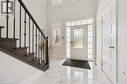 Bright entryway featuring white marble-look tile flooring, a white paneled entry door with frosted sidelights and transom windows, and a dark wood staircase with black iron balusters - 