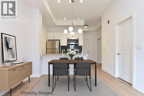 Open-concept living area with light wood-finish flooring, a contemporary chandelier, recessed lighting, and a kitchen featuring stainless steel appliances and white cabinetry - 4040 Upper Middle Road Unit# 105, Burlington, ON 