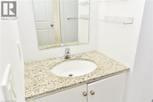 Vanity featuring a white oval sink, granite countertop, chrome faucet, white cabinetry, and brushed nickel hardware - 4040 Upper Middle Road Unit# 105, Burlington, ON 
