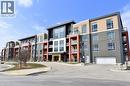 Contemporary multi-story building featuring varied facade materials including brick and paneling, multiple private balconies with glass railings, a ground-level garage entrance, and a curved paved dri - 4040 Upper Middle Road Unit# 105, Burlington, ON 