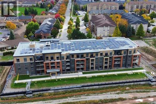 Modern multi-story building featuring an array of rooftop solar panels, multiple private balconies with glass railings, and a contemporary façade with varied exterior finishes - 4040 Upper Middle Road Unit# 105, Burlington, ON 