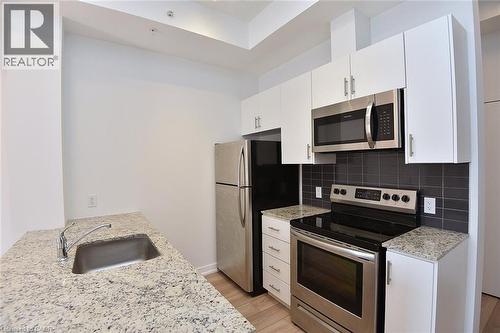 Modern kitchen featuring white cabinetry, light-colored speckled countertops, stainless steel appliances, dark subway tile backsplash, and light wood-finish flooring - 4040 Upper Middle Road Unit# 105, Burlington, ON 
