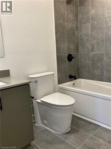 Bathroom featuring a white toilet, coordinating vanity with a light countertop, and a built-in bathtub with dark-toned wall tiling - 4878 Powers Common Unit# C-1105, Burlington, ON 