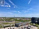 Expansive urban landscape featuring a retail plaza with multiple storefronts, a multi-story residential building, and a distant body of water - 4878 Powers Common Unit# C-1105, Burlington, ON 