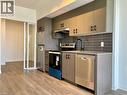 Contemporary kitchen featuring wood-finish flooring, stainless steel appliances, dark subway tile backsplash, matte black faucet, and two-tone cabinetry with dark hardware - 4878 Powers Common Unit# C-1105, Burlington, ON 
