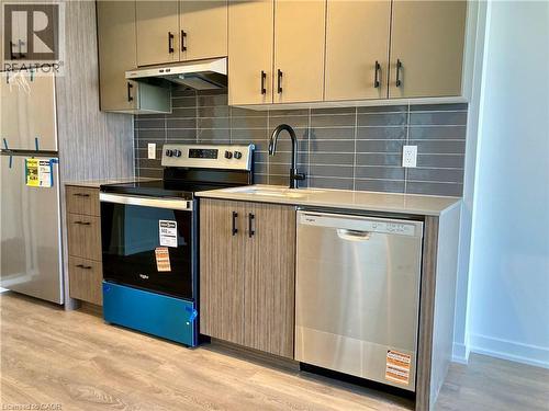 Modern kitchen featuring stainless steel appliances, grey subway tile backsplash, light-toned countertops, wood-finish flooring, and two-tone cabinetry with matte black hardware - 4878 Powers Common Unit# C-1105, Burlington, ON 