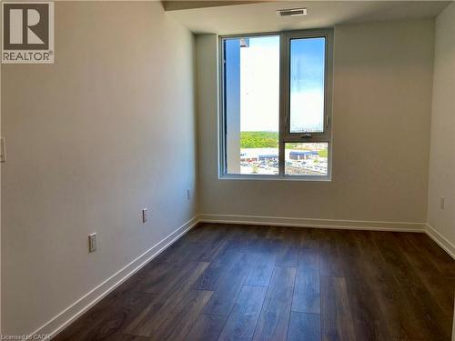 Room featuring wood-finish flooring, white baseboards, and a large window with silver-tone framing - 4878 Powers Common Unit# C-1105, Burlington, ON 