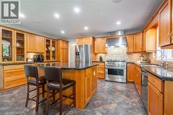 Kitchen featuring a kitchen bar, stainless steel appliances, a kitchen island, a sink, and wall chimney range hood - 
