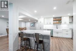 Kitchen featuring a kitchen bar, stainless steel appliances, white cabinetry, a sink, and wall chimney range hood - 