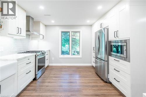 Kitchen with appliances with stainless steel finishes, light wood-type flooring, light stone counters, wall chimney range hood, and backsplash - 18 Westie Road, Brantford, ON 