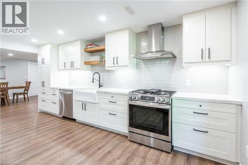 Kitchen featuring backsplash, open shelves, appliances with stainless steel finishes, wall chimney range hood, and light wood-style floors - 18 Westie Road, Brantford, ON 