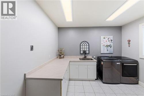 Laundry room featuring a built-in utility sink with a black faucet, white cabinetry, extensive countertop space, washer and dryer and tile flooring - 7775 St. Augustine Crescent, Niagara Falls, ON 
